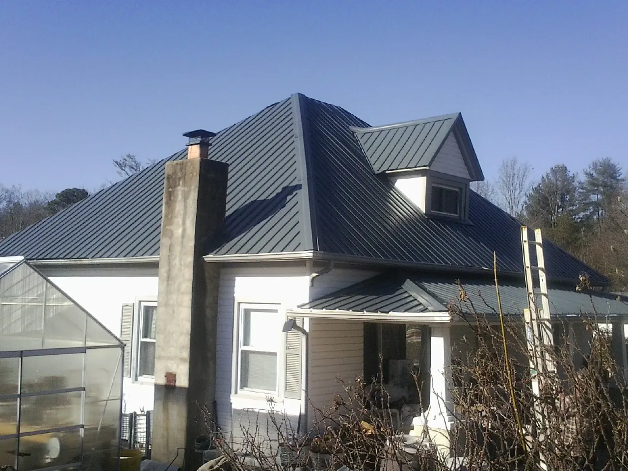 Dark blue standing seam metal roof on a white farmhouse with dormer — Slate & Tile Roof Repair by Roofing Brothers in Mooresville