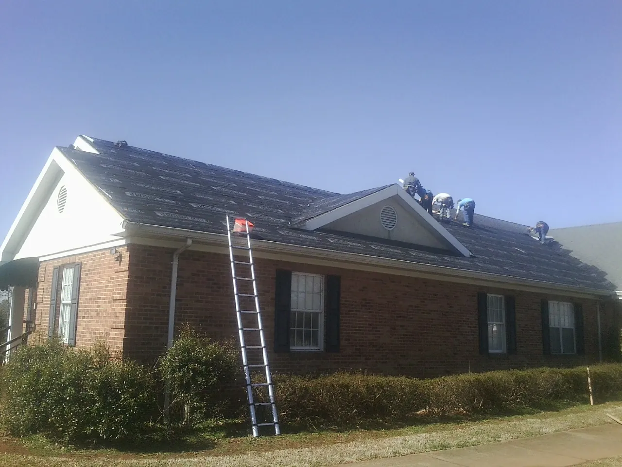 Crew tearing shingles off a brick ranch roof with a ladder set — Emergency Roof Repair work by our crew in Mooresville