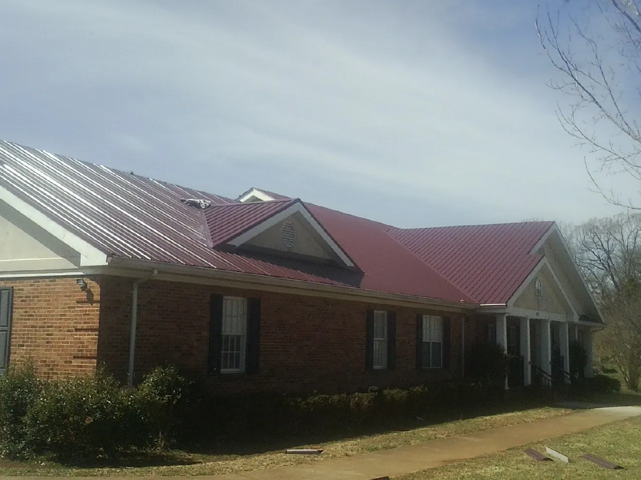 Red metal roof with gabled entries on a long brick building, from a Hail Damage Roof Repair job in Mooresville