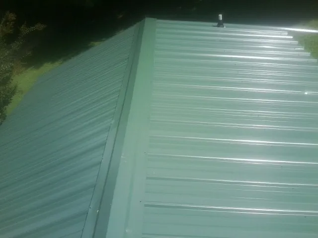 New green metal panels meeting at the ridge of a roof — Flat Roof Repair work by our crew in Mooresville